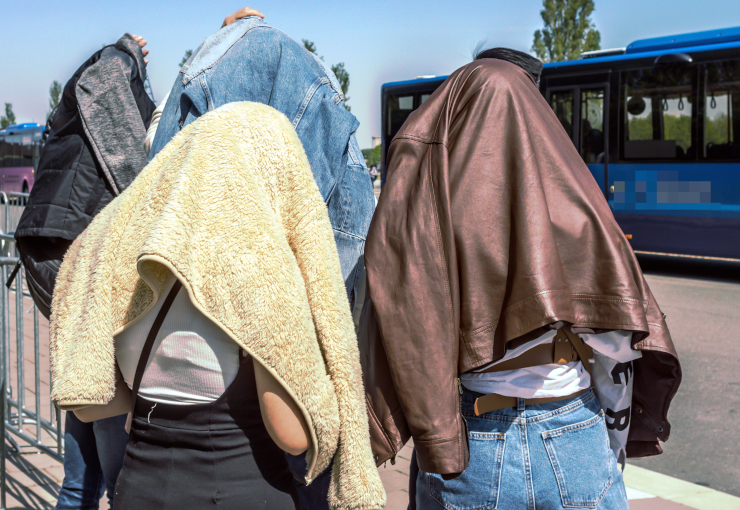 People waiting at a bus stop with clothing over their heads, looking (vaguely) like ghosts