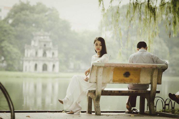 A person on a bench facing away from the other person and the scenery to look into the middle distance